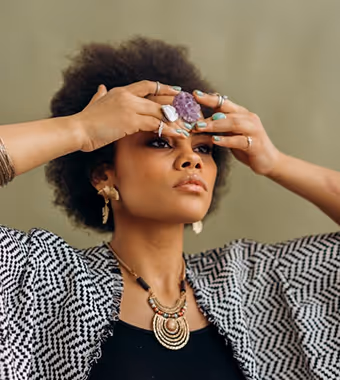 A stylish Black woman holds her hands over her forehead with a crystal between.
