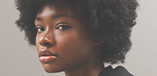 A close-up, artistic profile shot of a Black woman with natural hair, looking thoughtfully off-camera.