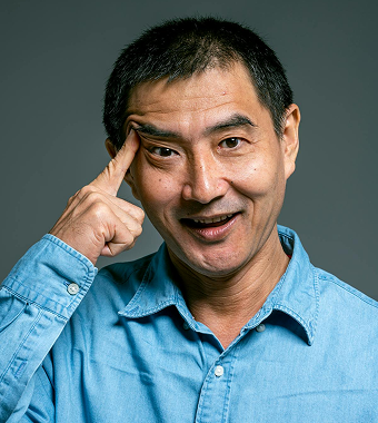 A man in a blue shirt smiles and points to his temple.