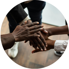 A circular photo showing a stack of many diverse hands on top of one another, symbolizing teamwork and unity.