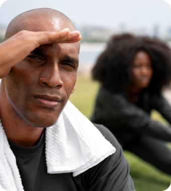 An older Black man with a towel around his neck shields his eyes with his hand as he looks thoughtfully into the distance.