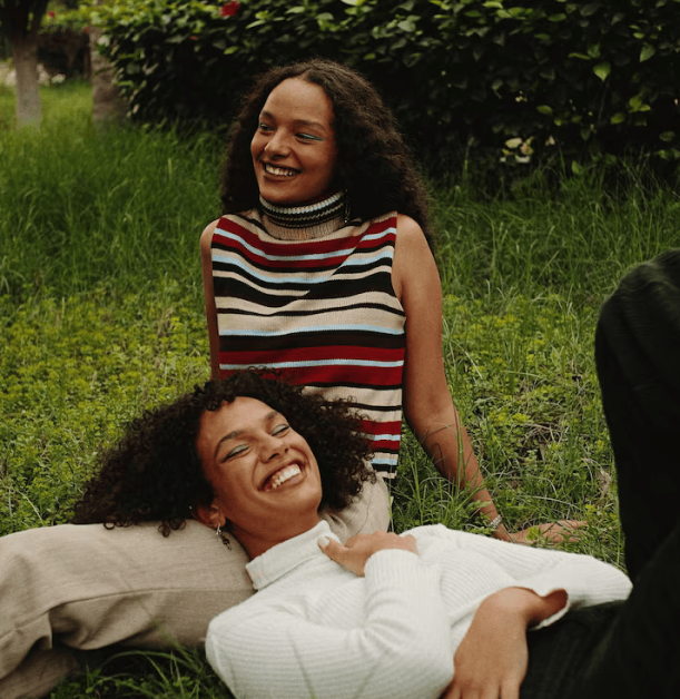 Two women sitting in the grass, smiling and laughing.