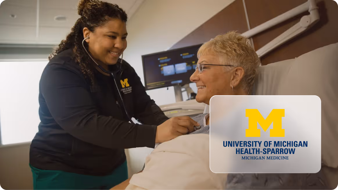 Smiling healthcare worker with a stethoscope checking the heart of a female patient lying in a hospital bed.