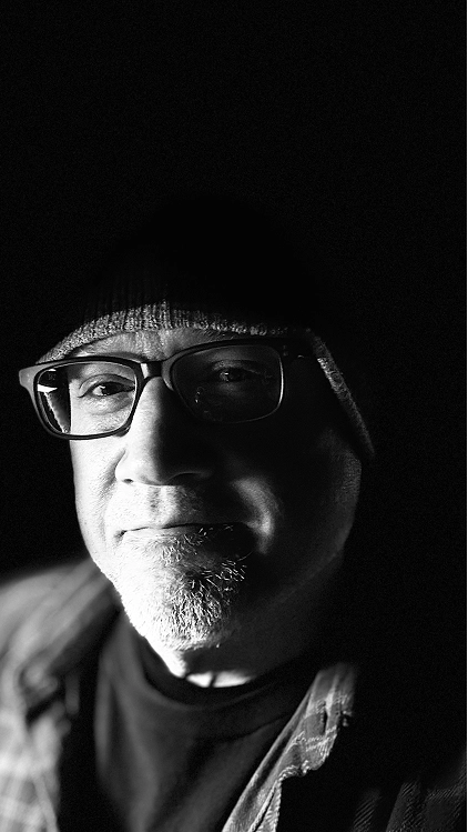 Black-and-white close-up portrait of a man wearing glasses and a beanie in low light.