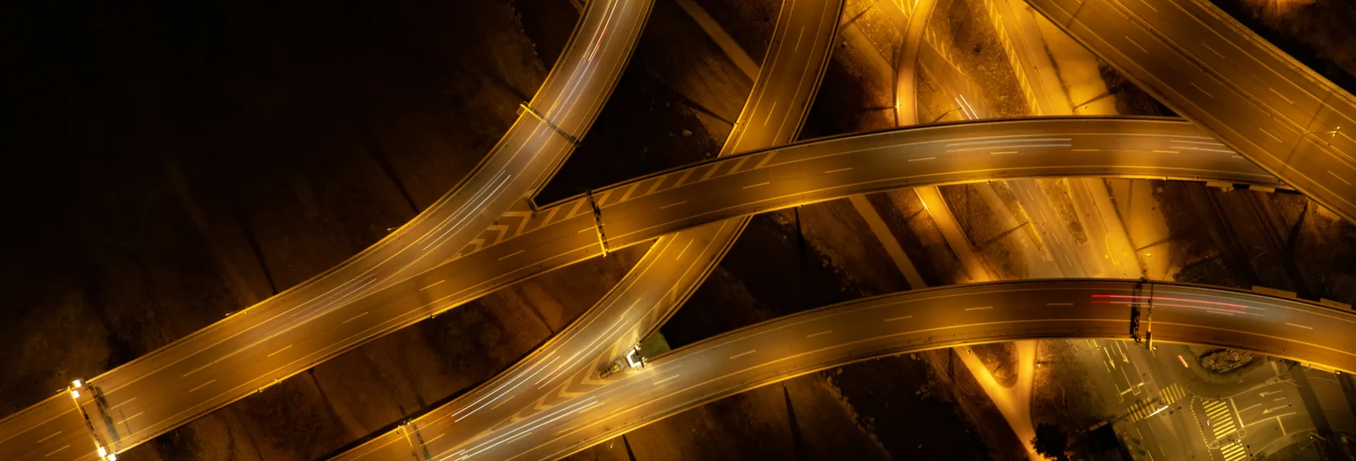Aerial view of illuminated intertwined highways at night with light trails from vehicles.