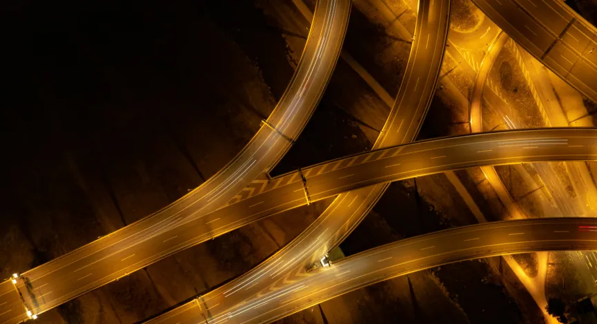 Aerial view of illuminated curving highway interchange at night with light trails from vehicles.