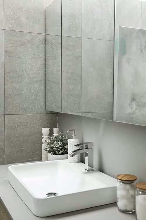 close up of a bathroom sink on a grey counter with grey tiled walls and a mirror medicine cabinet