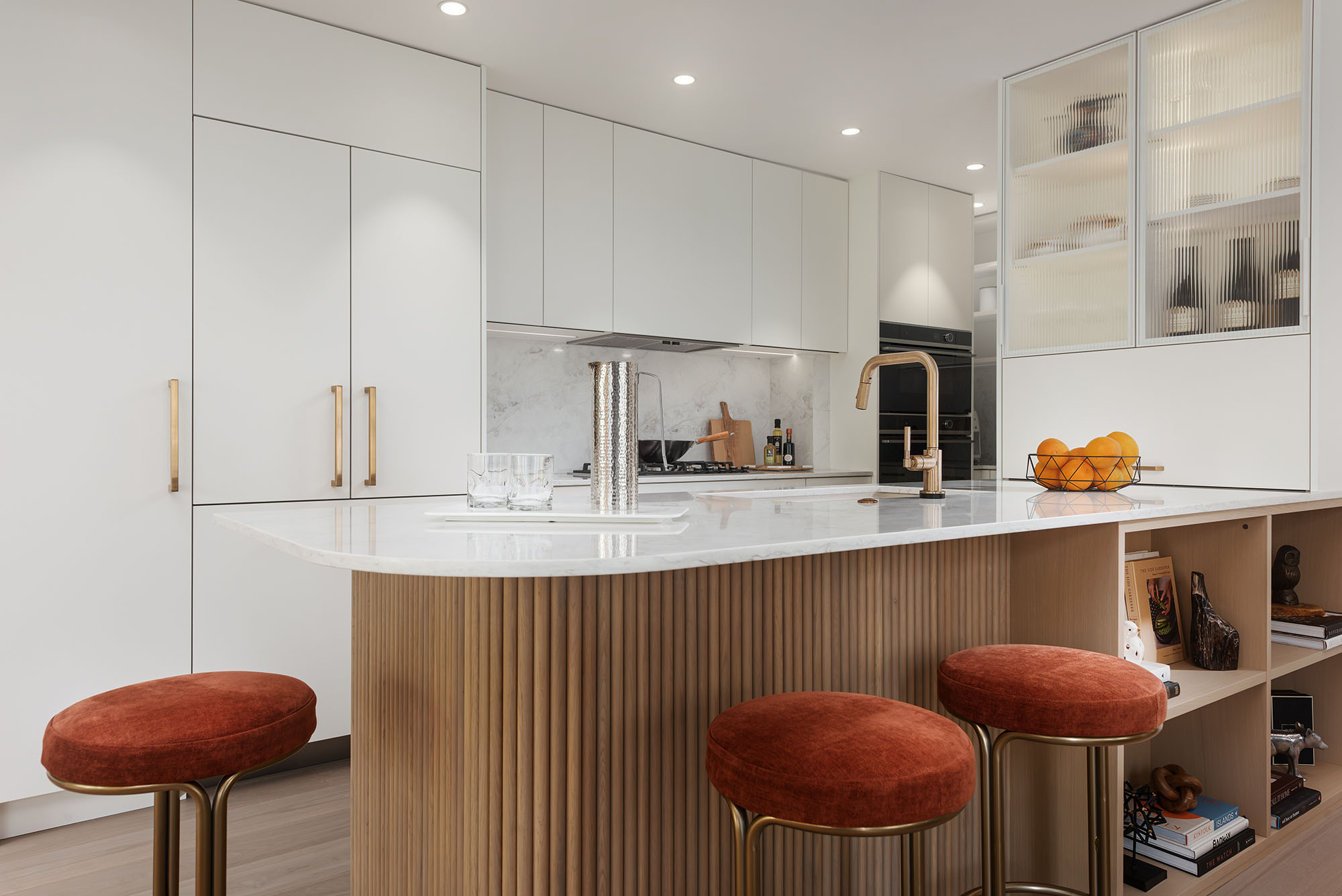 Modern kitchen corner with white marble countertops, a black glass cabinet, wooden and marble cutting boards, a potted plant, candles, and a stainless steel gas stove.