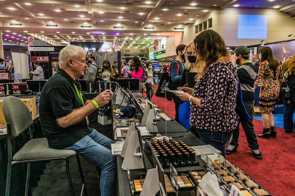 a person talking to someone at their make up booth on the expo floor