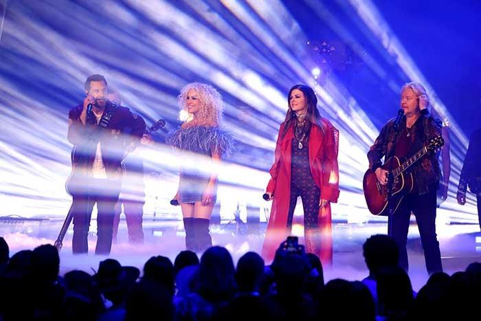 Four performers stand in white beams of light in front of an audience