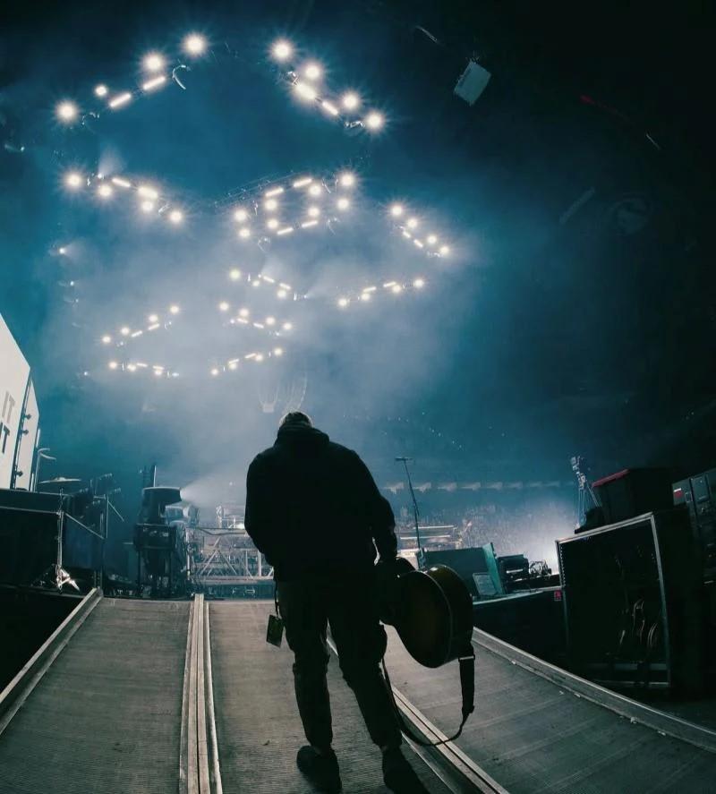 A musician hold a guitar in their right hand and walks onto the stage at Winter Jam 2025.