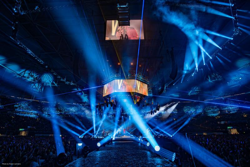 Dark stadium with circular stage encompassed in blue beaming lights.