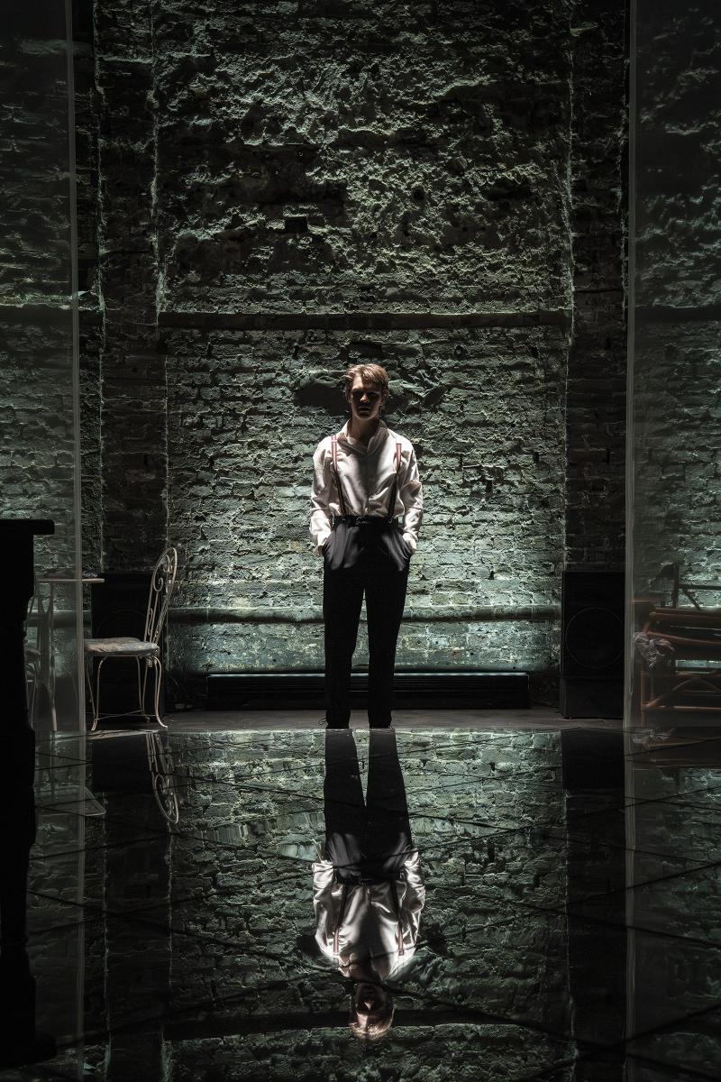 A dark haunting lit stage with a single man standing in the center backlit.