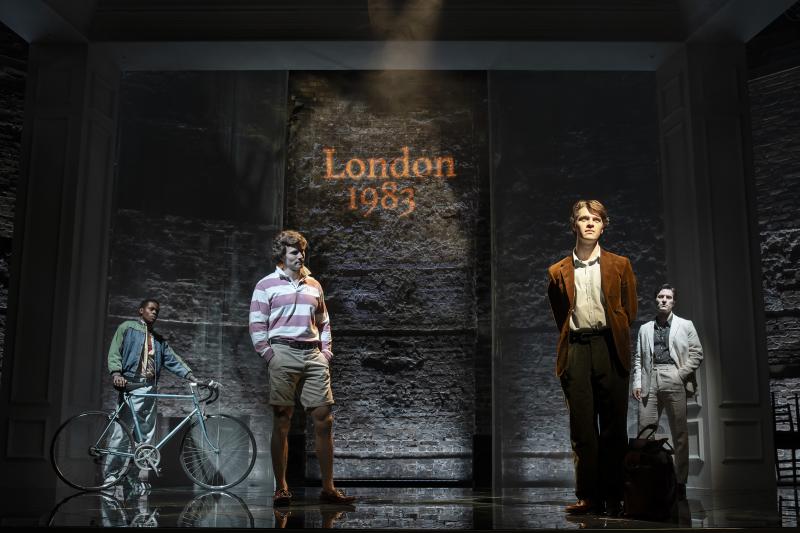 A dark hued London 1983 themed stage with 4 individuals standing facing the crowd.