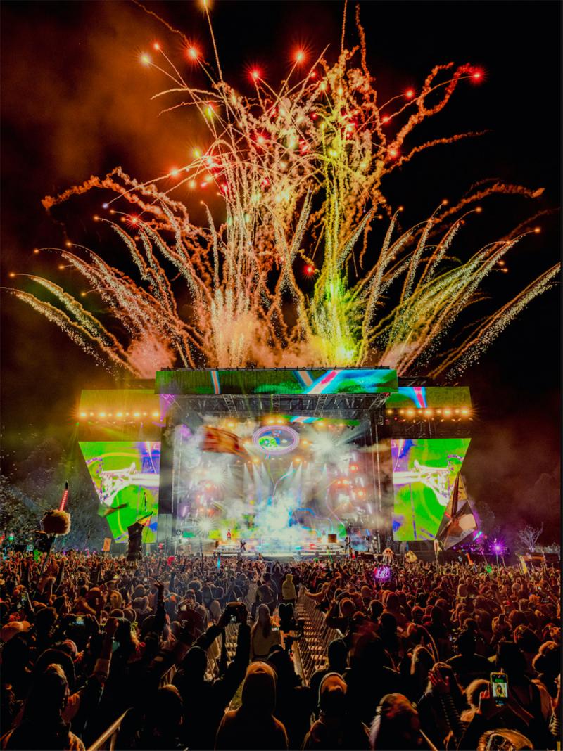 A concert stage with an audience in the foreground and fireworks behind it