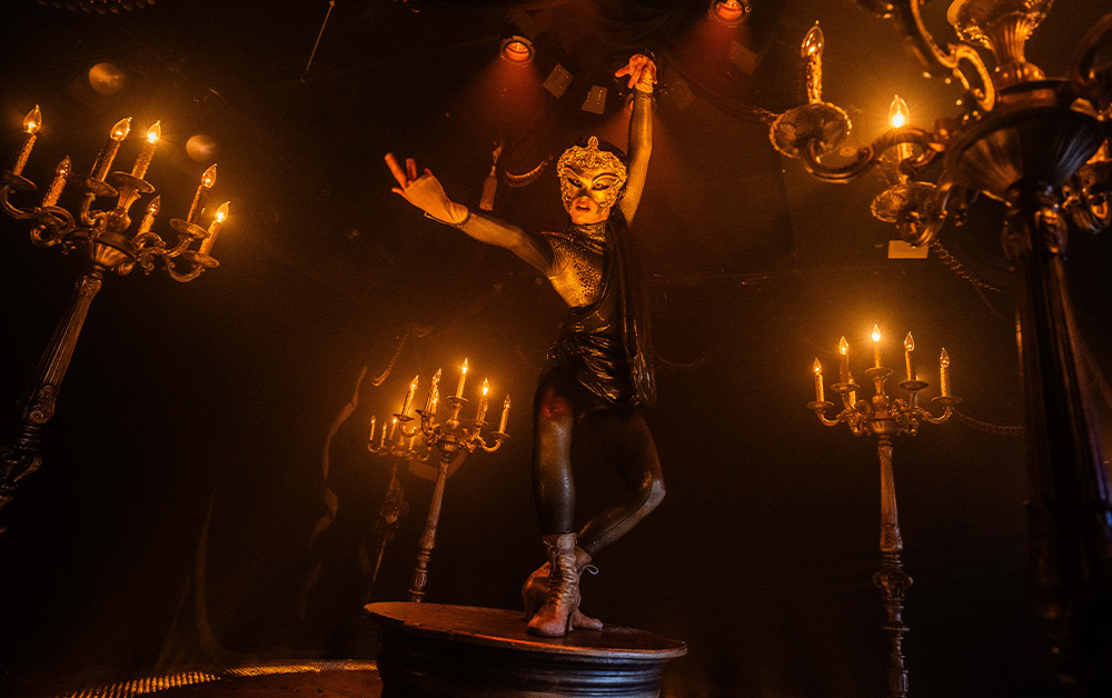 A person in a garment standing on a round table with candlesAI-generated content may be incorrect.