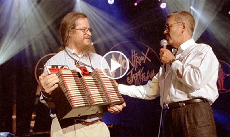 Two men onstage with a video player button over them