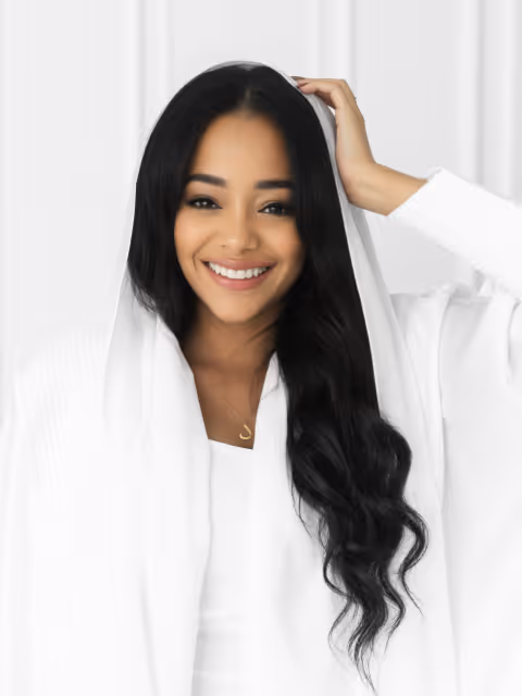 Smiling woman with long black hair wearing a white hooded garment against a white background.
