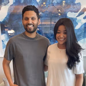 Smiling man and woman standing side by side indoors with abstract blue artwork in the background.