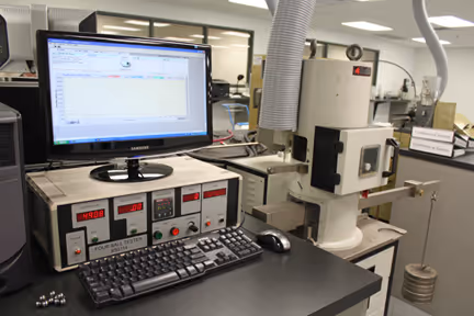 Laboratory setup at Loadmaster Lubricants with a computer displaying a graph, connected to a precision testing device with control panels and a keyboard on a black table.
