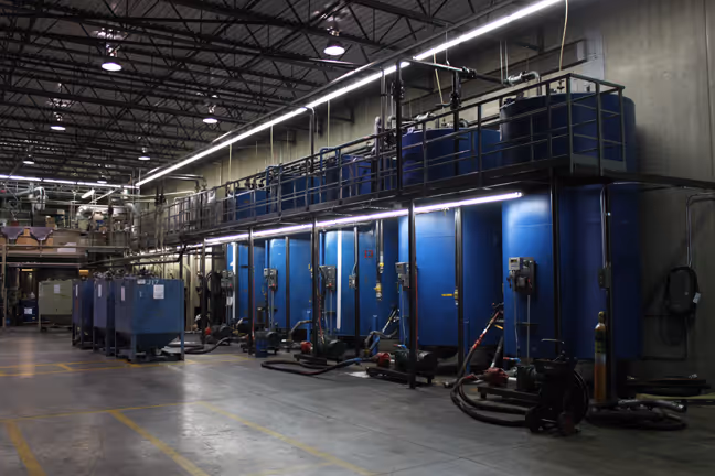 Loadmaster grease Industrial facility interior with blue storage tanks aligned against a wall and connected piping, pumps, and equipment