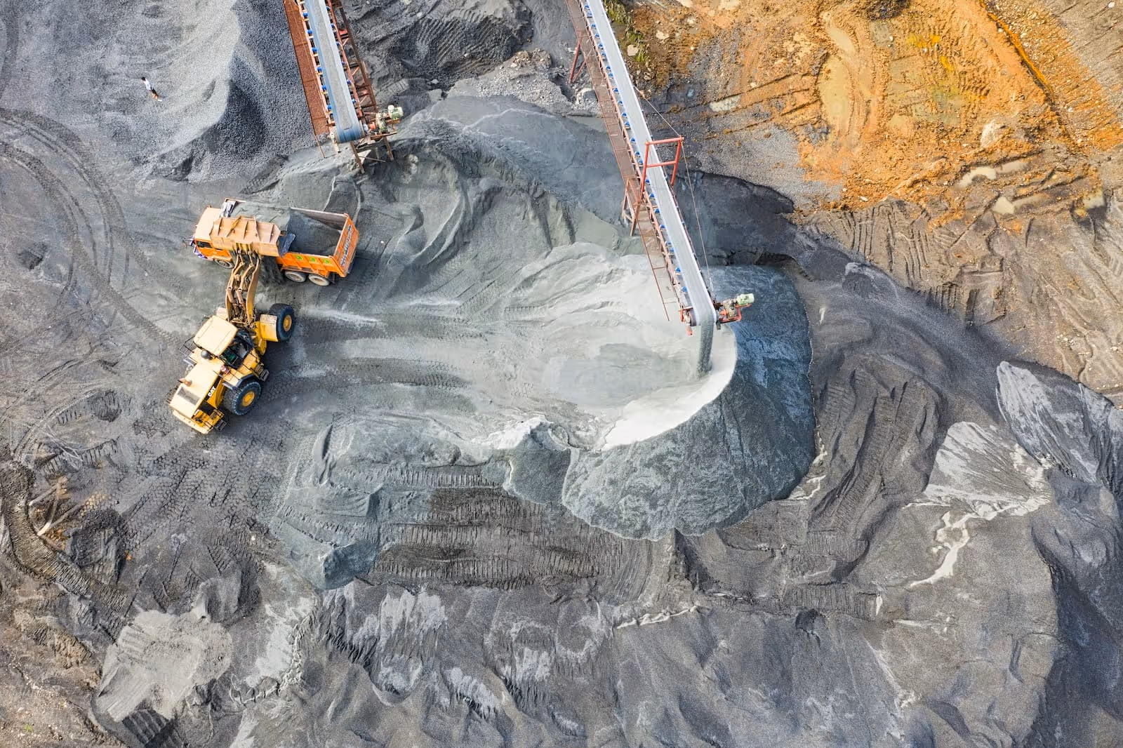Aerial view of construction machinery loading gravel into a dump truck at a mining site with conveyor belts depositing material.
