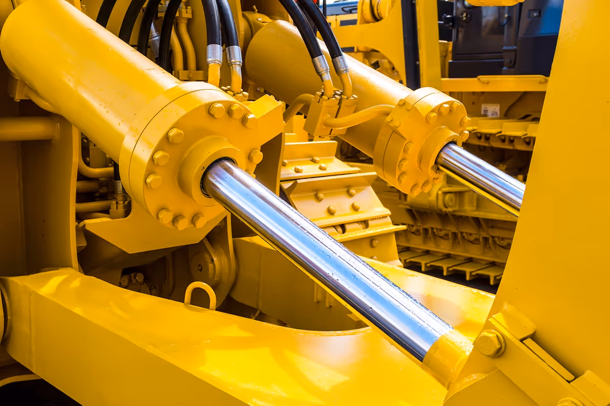 Close-up of hydraulic pistons with shiny metal rods on yellow heavy machinery.