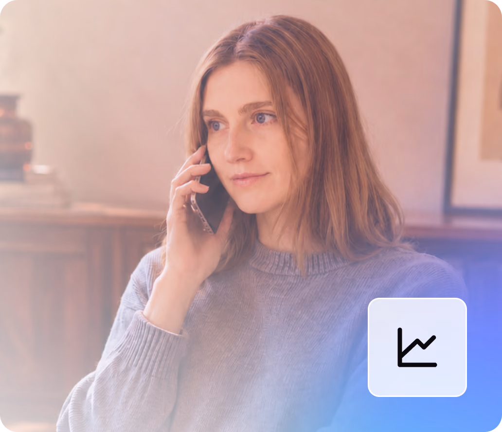 Woman with long hair wearing a gray sweater talking on a smartphone indoors.
