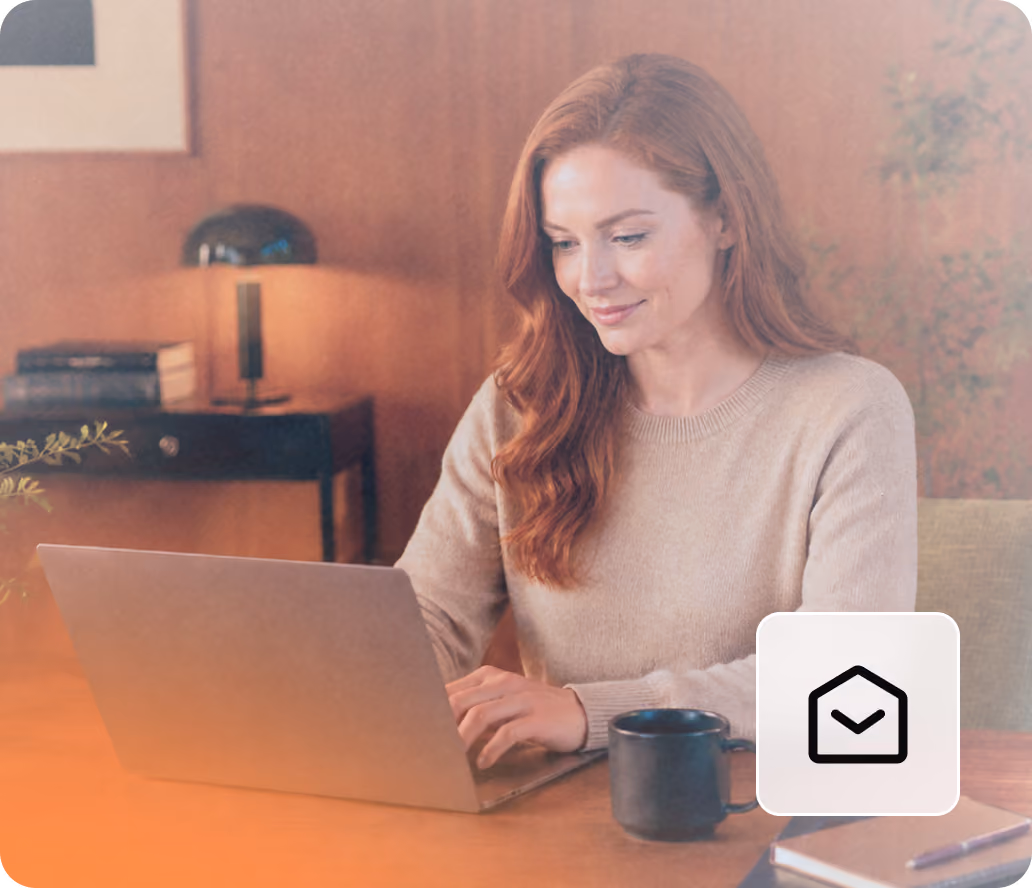 Woman with red hair working on a laptop at a wooden table with a black coffee mug nearby.