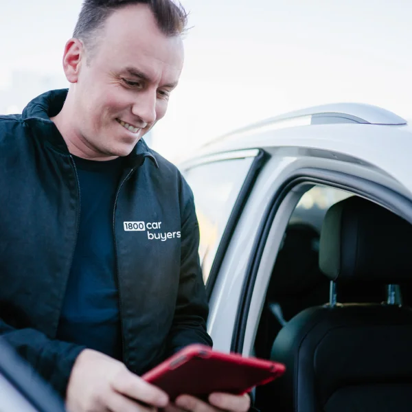 Smiling employee with tablet standing next to white car
