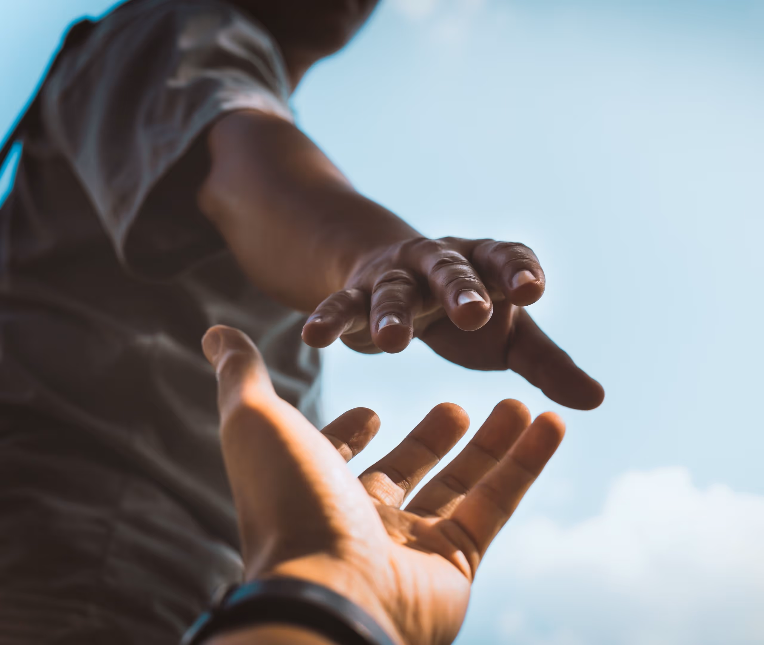Zwei Hände, die sich vor blauem Himmel fast berühren, symbolisieren Hilfe und Verbindung.
