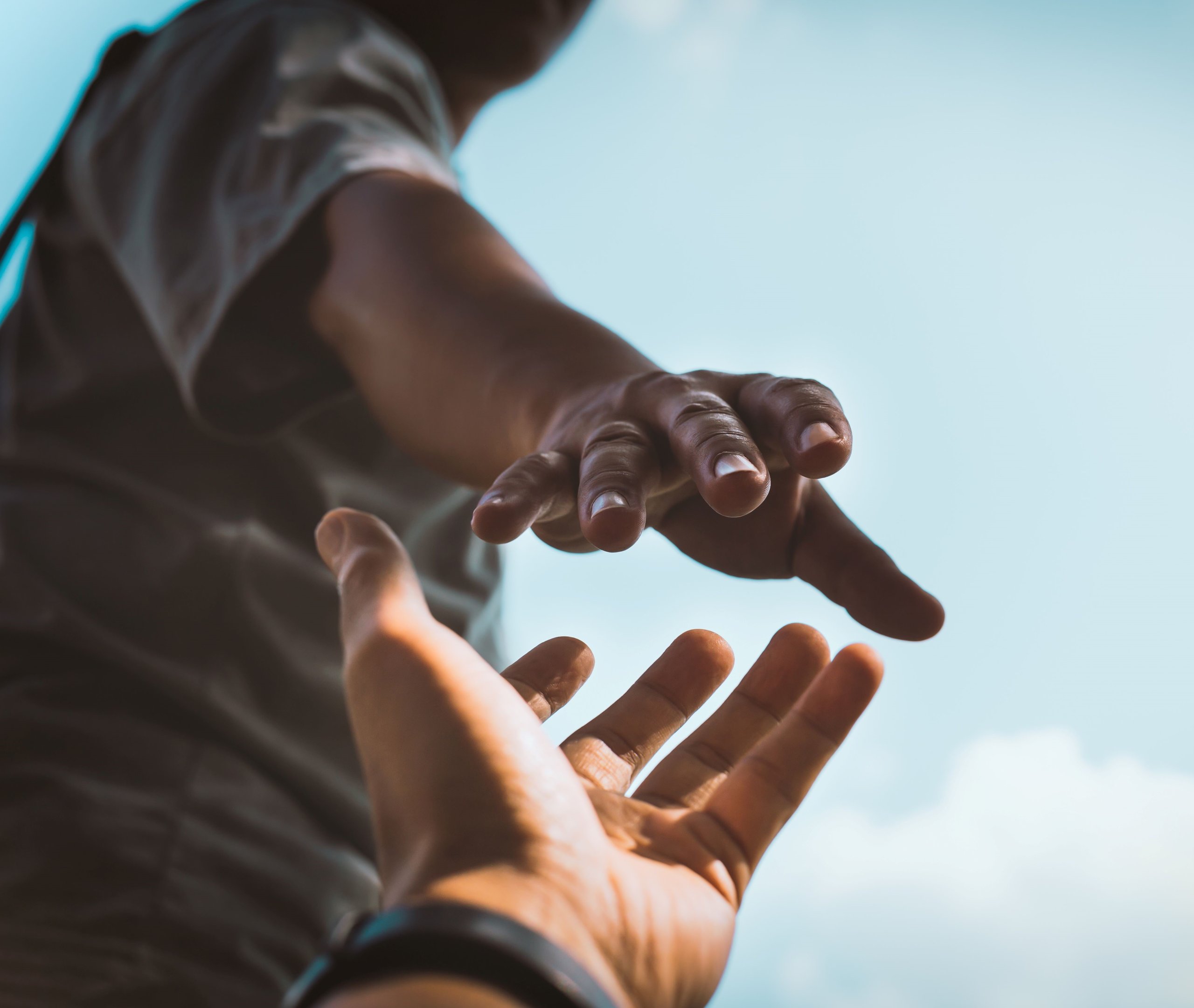 Zwei Hände, die sich vor blauem Himmel fast berühren, symbolisieren Hilfe und Verbindung.
