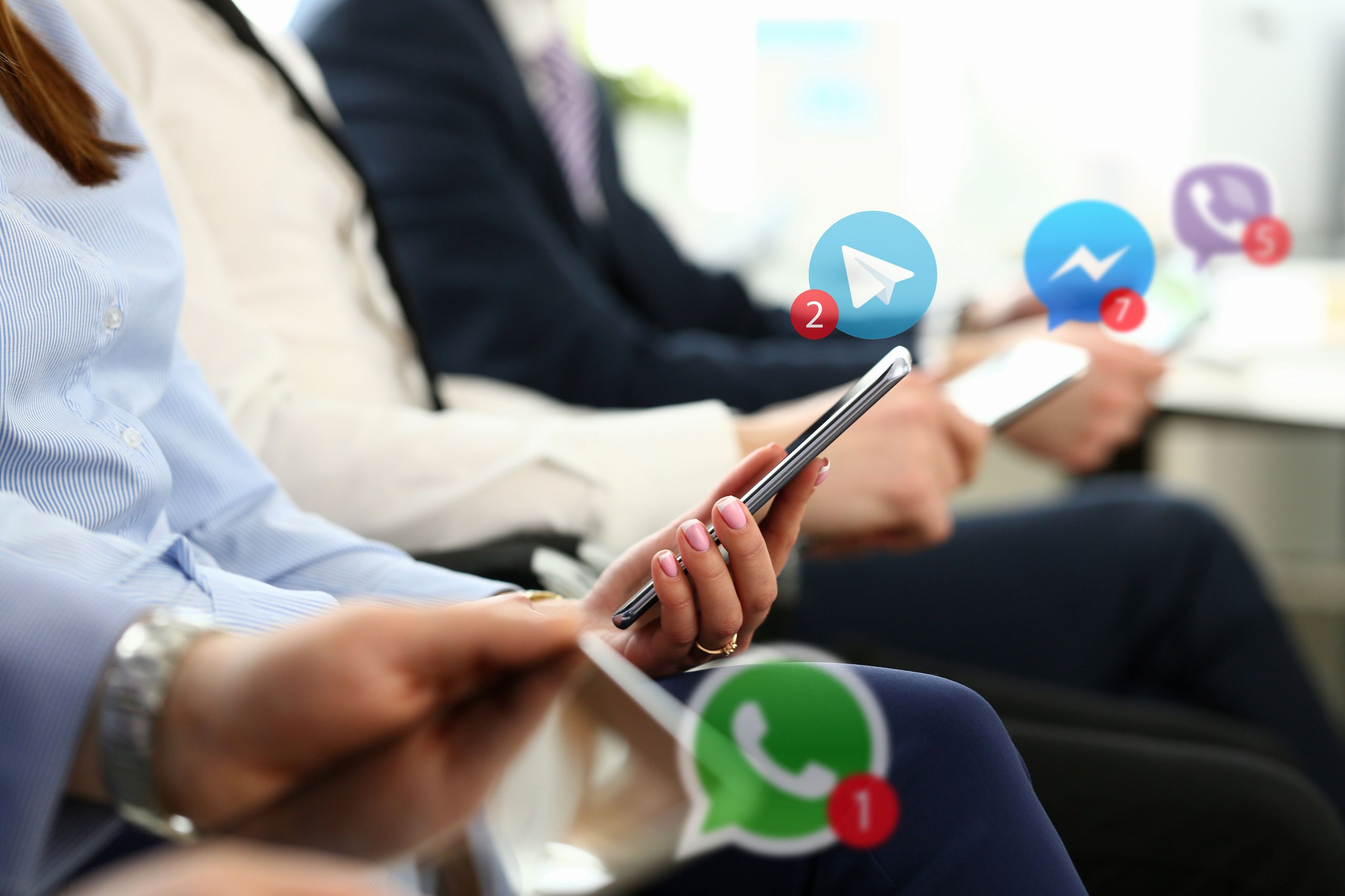 Vier Personen halten Smartphones in der Hand, auf denen Symbole von Telegram, Facebook Messenger, Viber und WhatsApp mit Benachrichtigungszählen angezeigt werden.