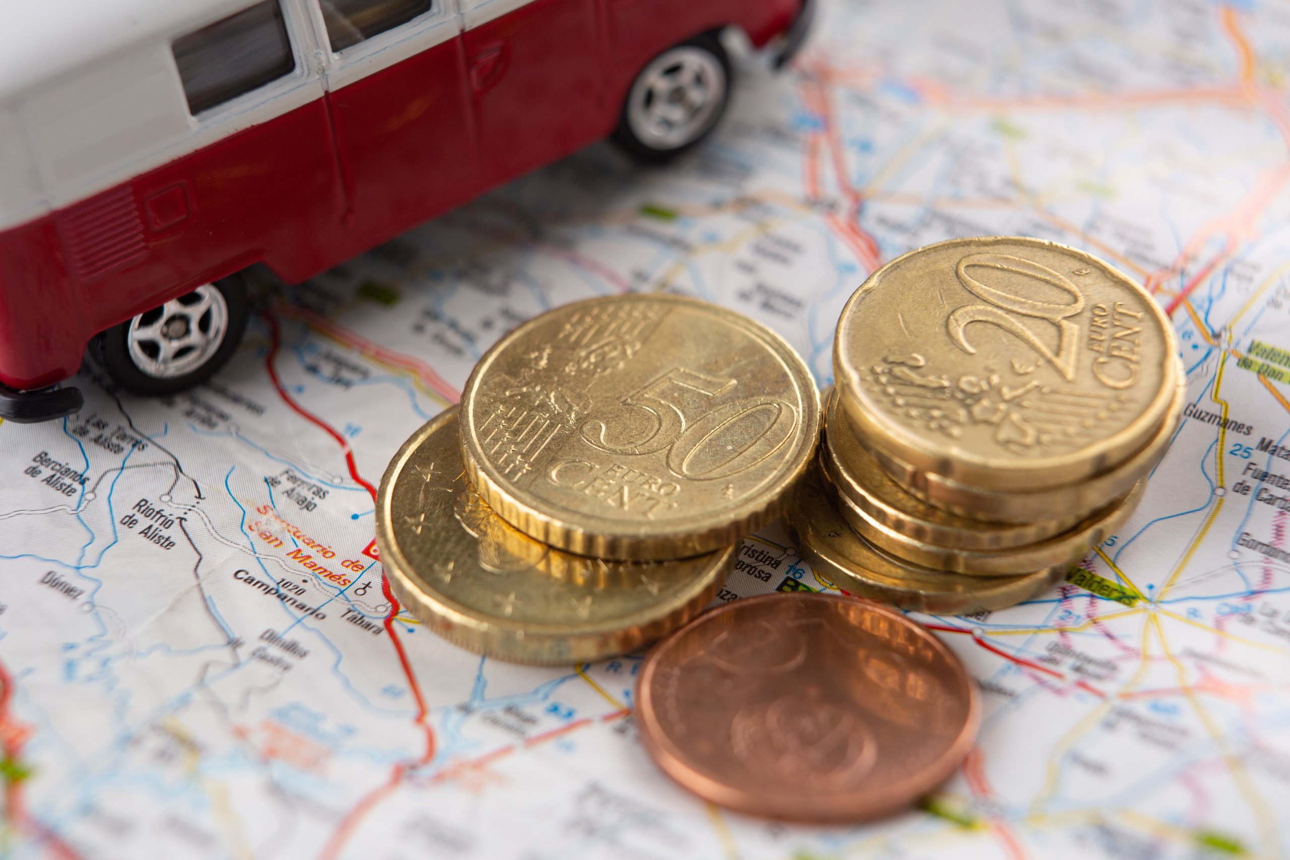 Euromünzen neben einem roten und weissen Spielzeugwagen auf einer Landkarte.