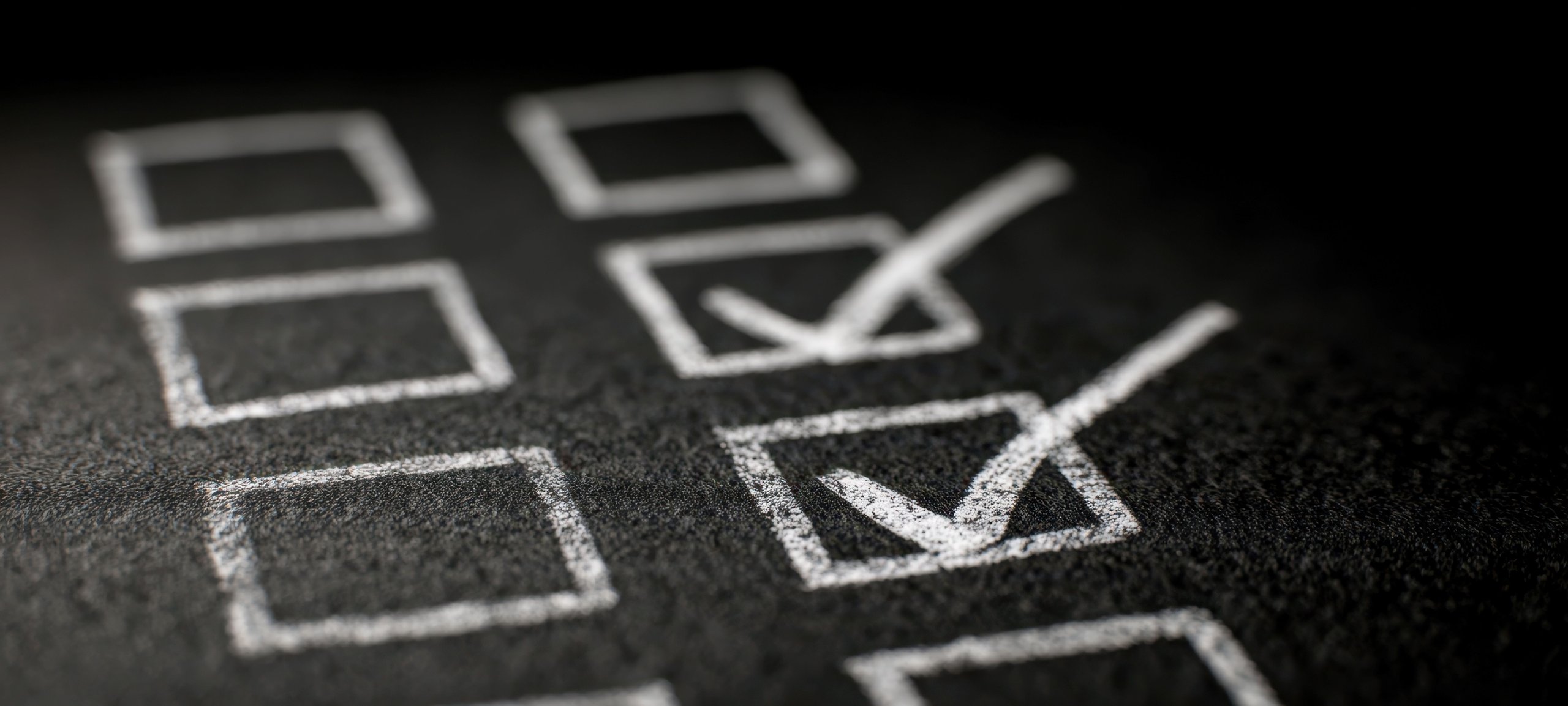 Zwei mit Kreide markierte Kästchen auf einer Tafel sind mit einem Häkchen versehen.