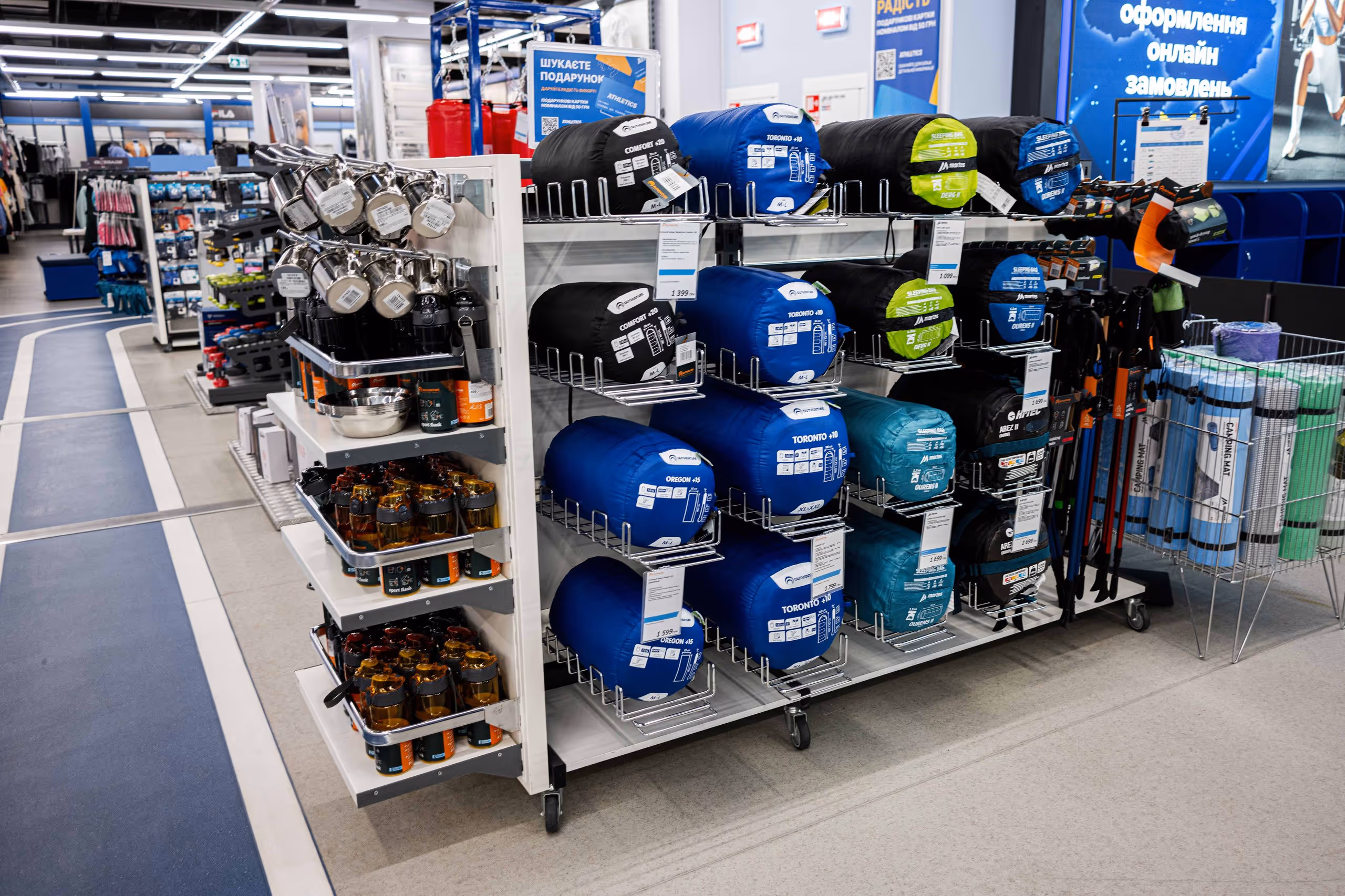 Regal mit zusammengerollten Schlafsäcken, Wasserflaschen und Wanderstöcken in einem Sportgeschäft.