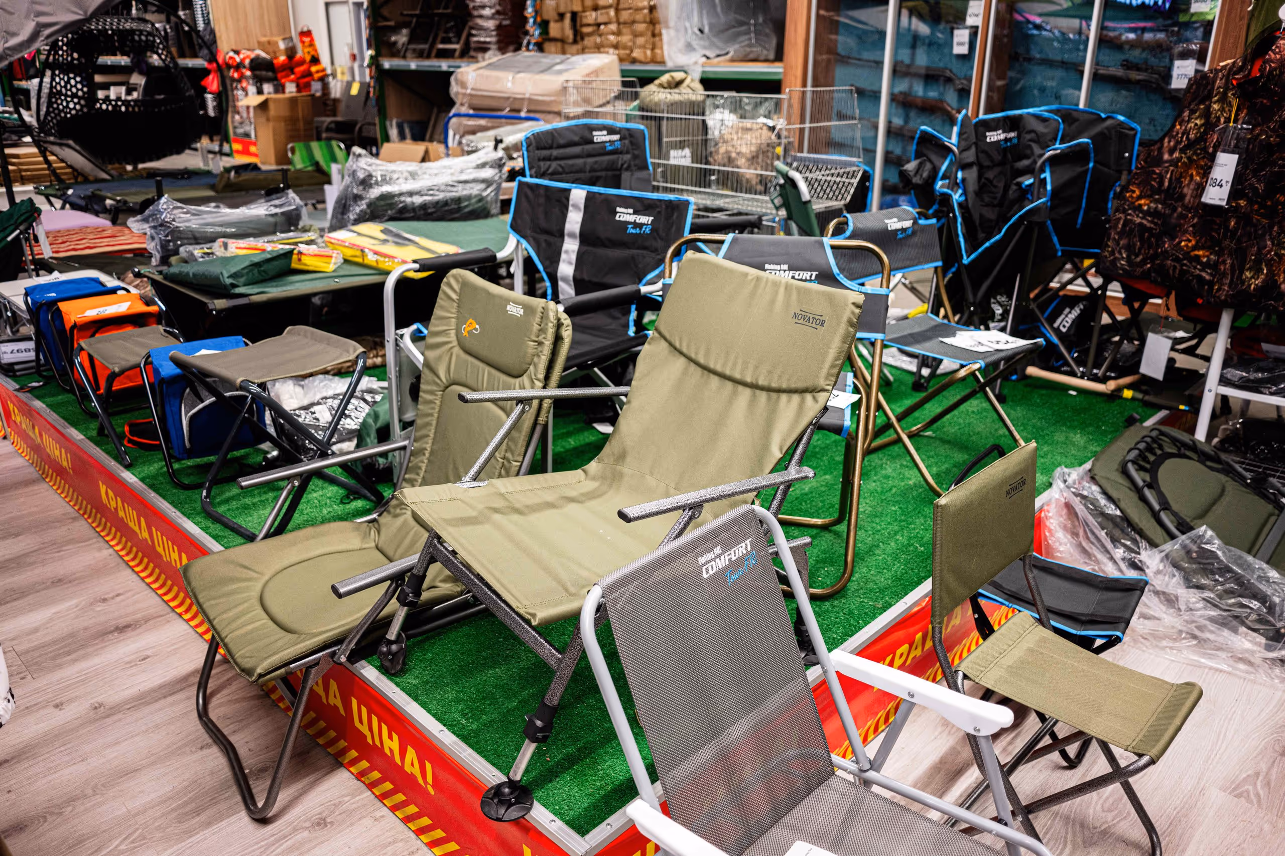 Verschiedene Campingstühle und Outdoor-Möbel in einem Laden auf grünem Teppichboden ausgestellt.