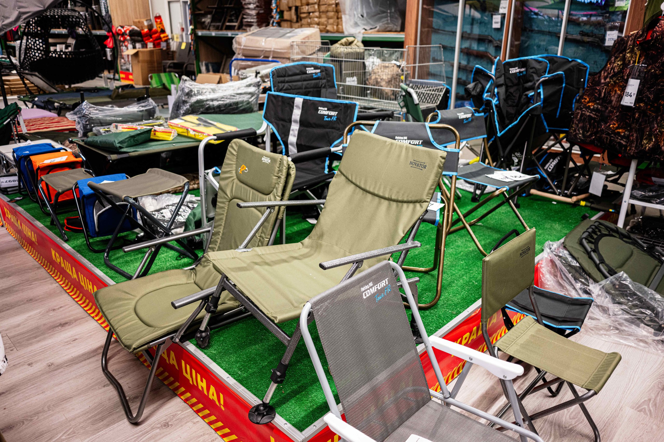 Verschiedene Campingstühle und Outdoor-Möbel in einem Laden auf grünem Teppichboden ausgestellt.