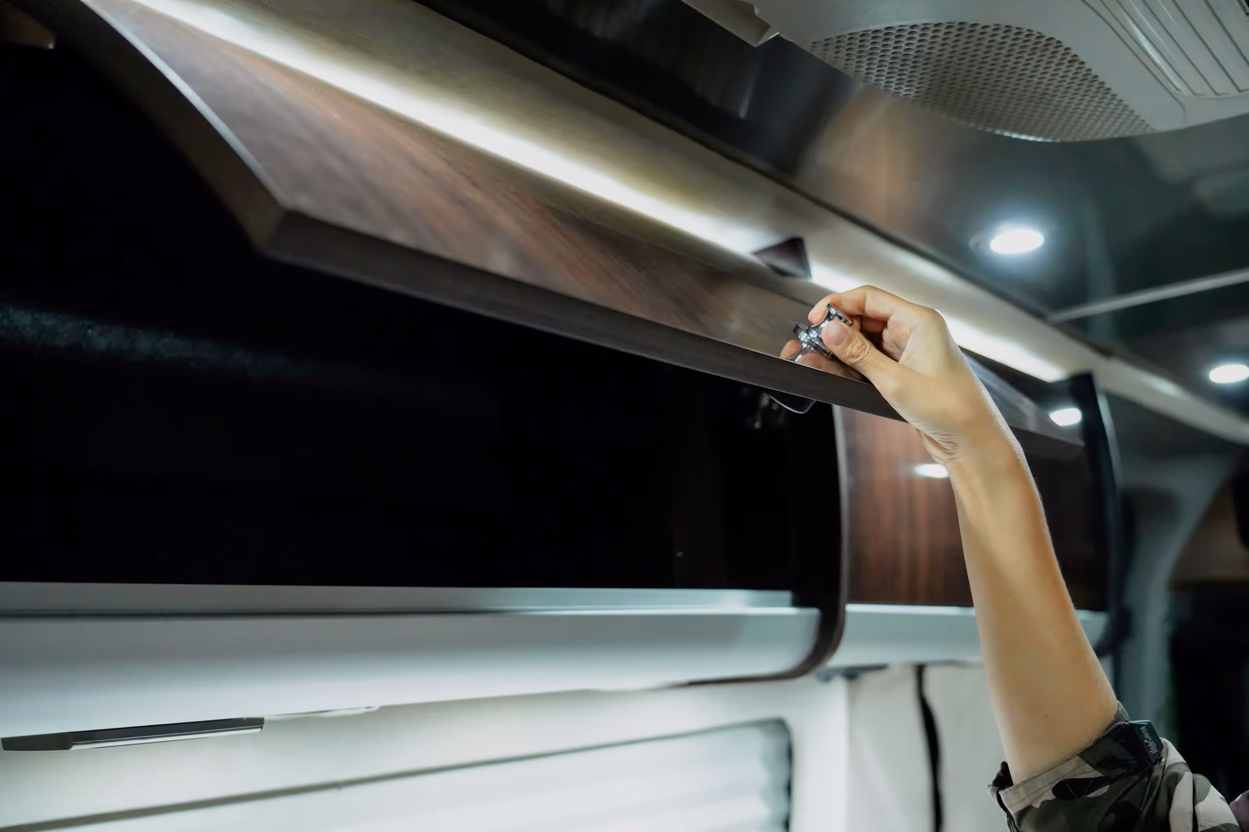 Hand öffnet einen dunkelbraunen Wandschrank mit Griff in einem modernen Innenraum.