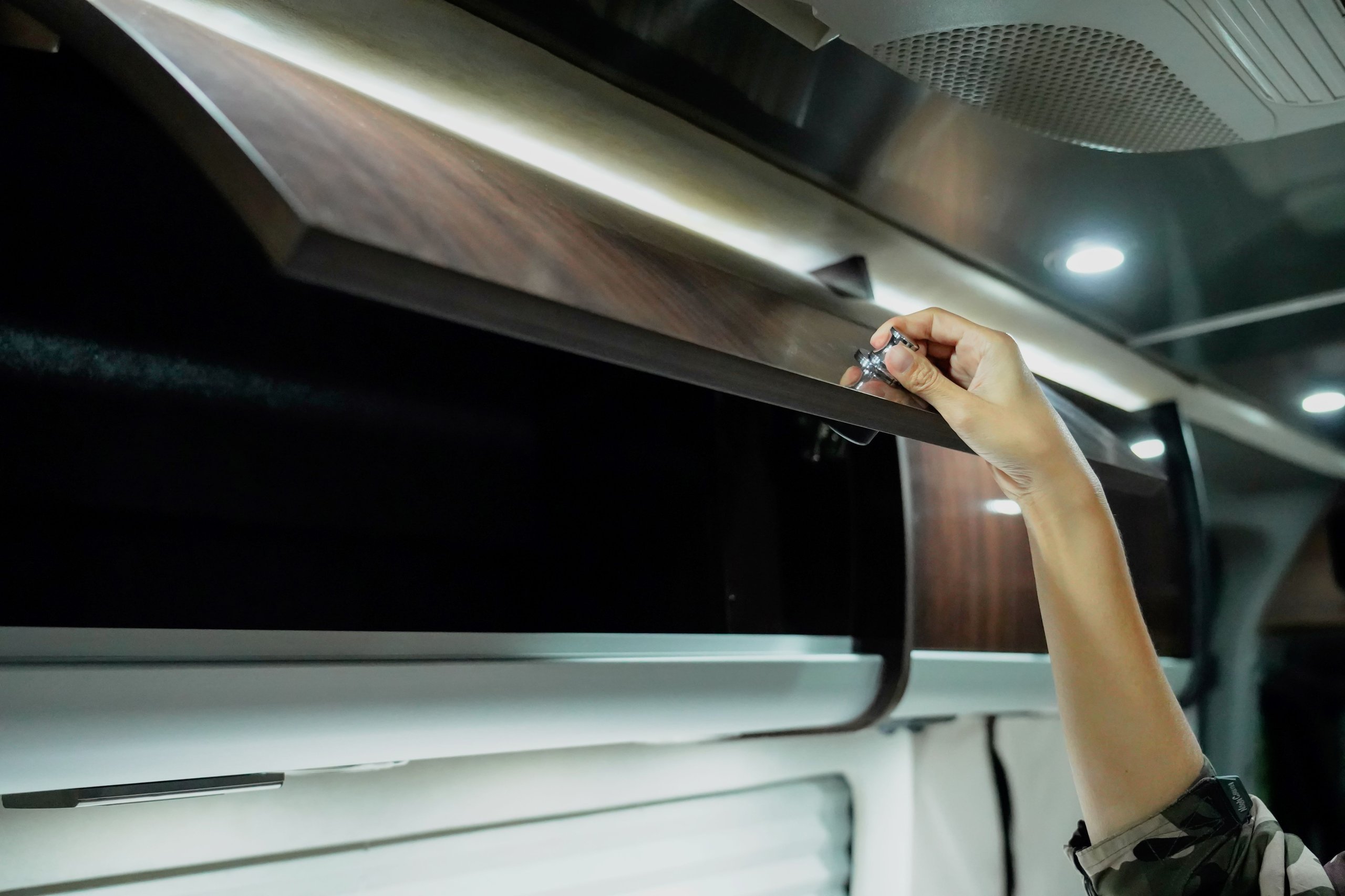 Hand öffnet einen dunkelbraunen Wandschrank mit Griff in einem modernen Innenraum.