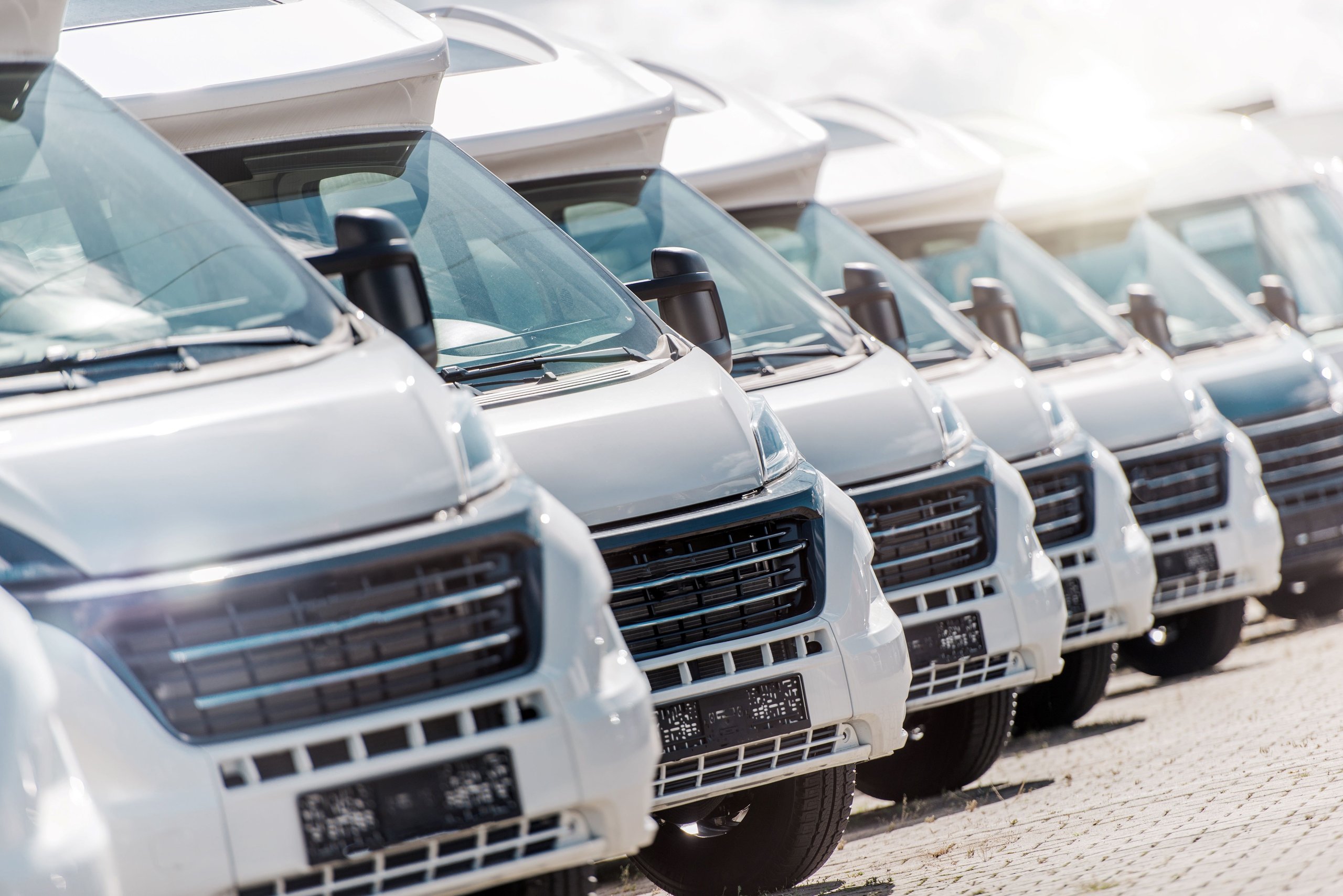Reihe von weißen Lieferwagen mit aufgestellten Dachfenstern auf gepflastertem Parkplatz.