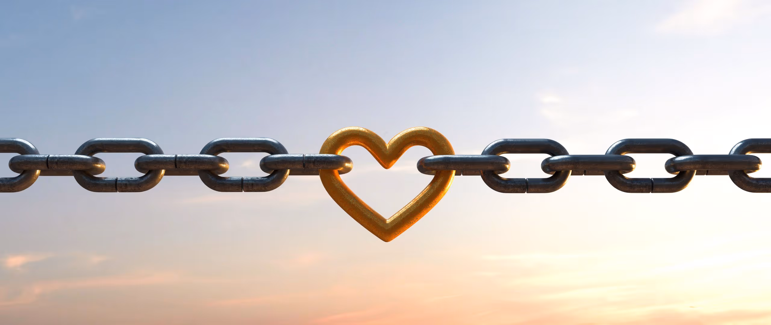 Metallkette mit einem goldfarbenen herzförmigen Glied in der Mitte vor einem Himmel bei Sonnenuntergang.
