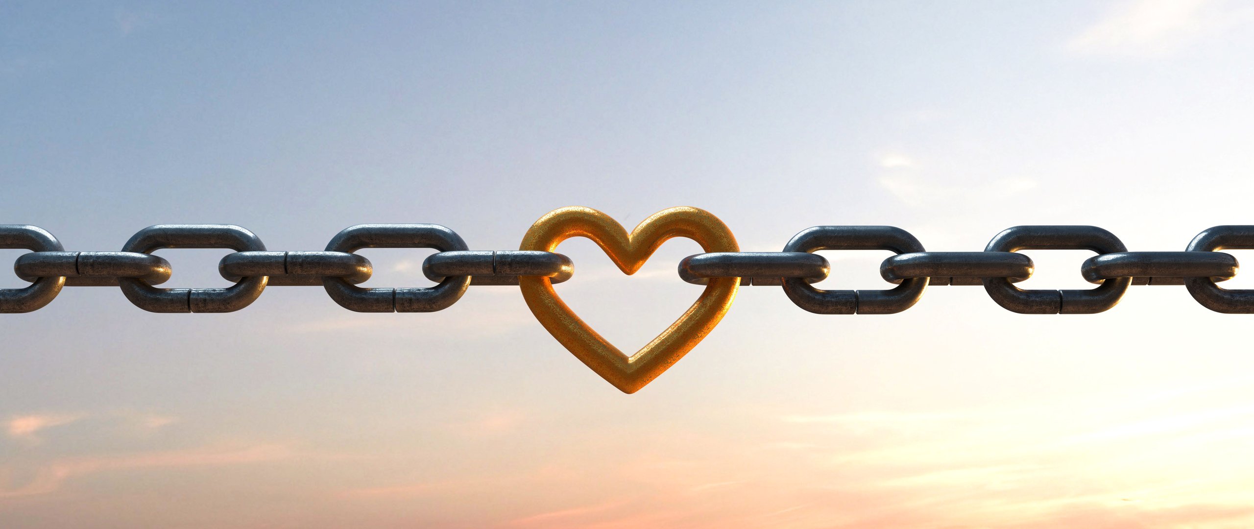 Metallkette mit einem goldfarbenen herzförmigen Glied in der Mitte vor einem Himmel bei Sonnenuntergang.