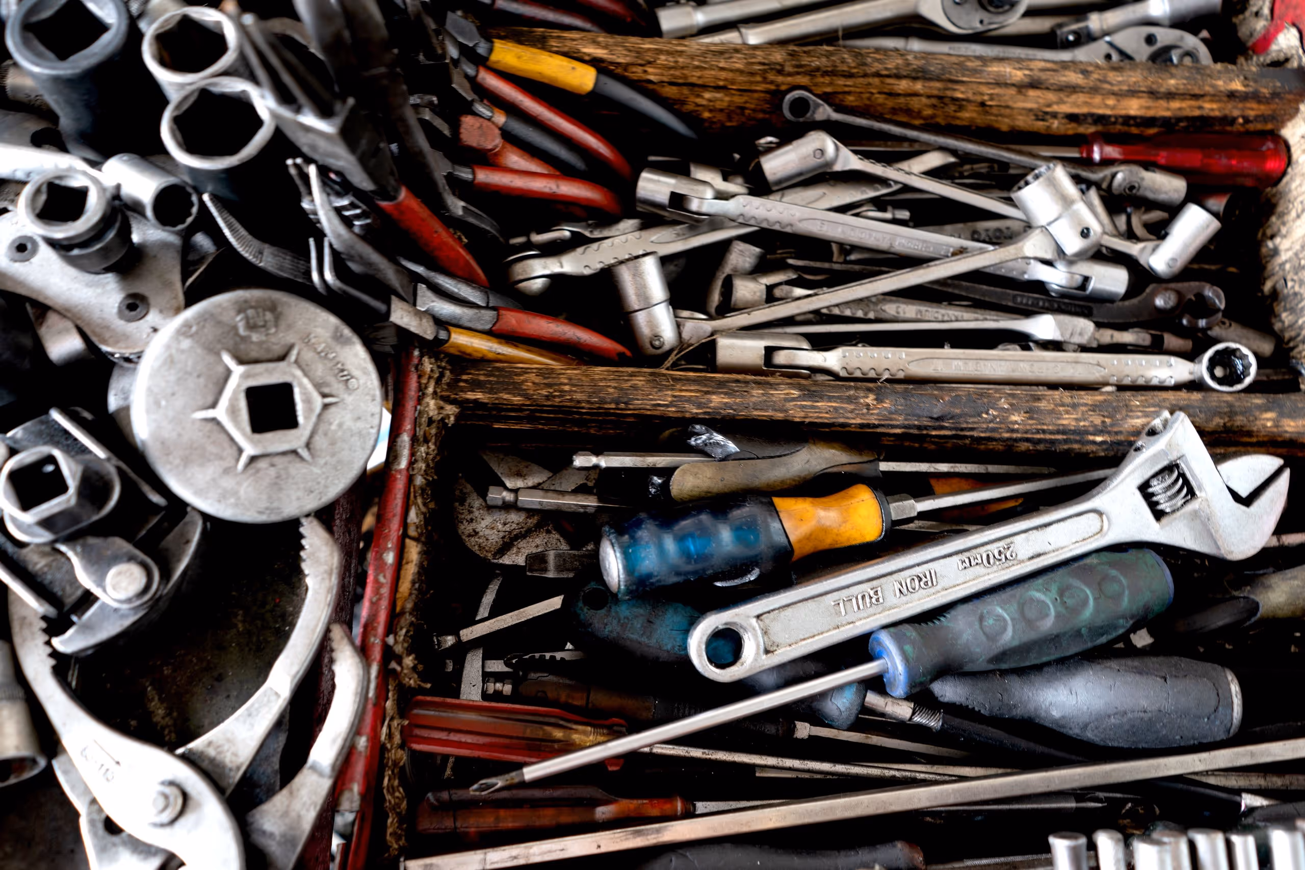 Eine Schublade mit verschiedenen Werkzeuge wie Schraubenschlüssel, Schraubendreher, Zangen und Nüsse, teilweise mit abgenutzten Griffen.