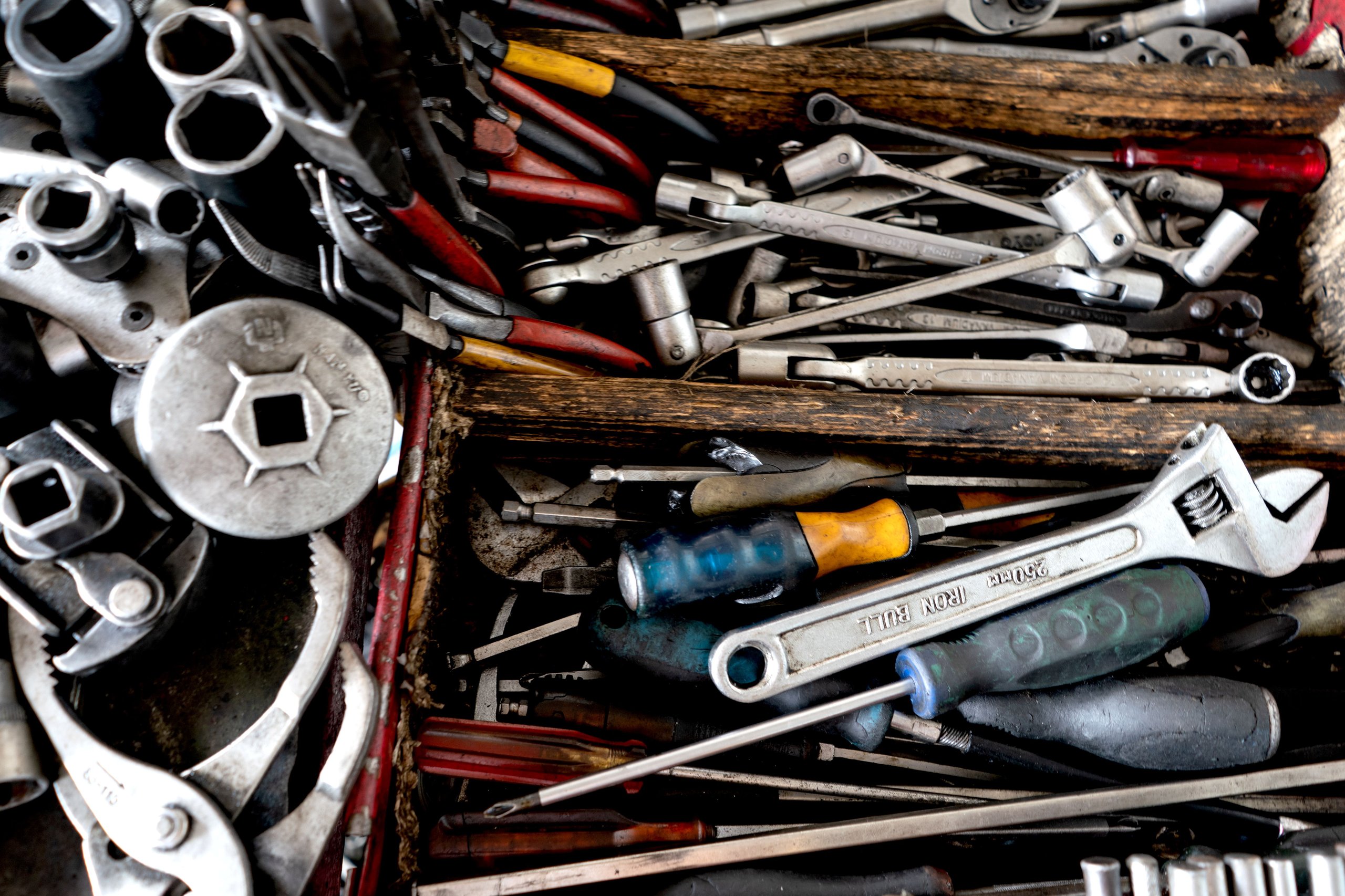 Eine Schublade mit verschiedenen Werkzeuge wie Schraubenschlüssel, Schraubendreher, Zangen und Nüsse, teilweise mit abgenutzten Griffen.