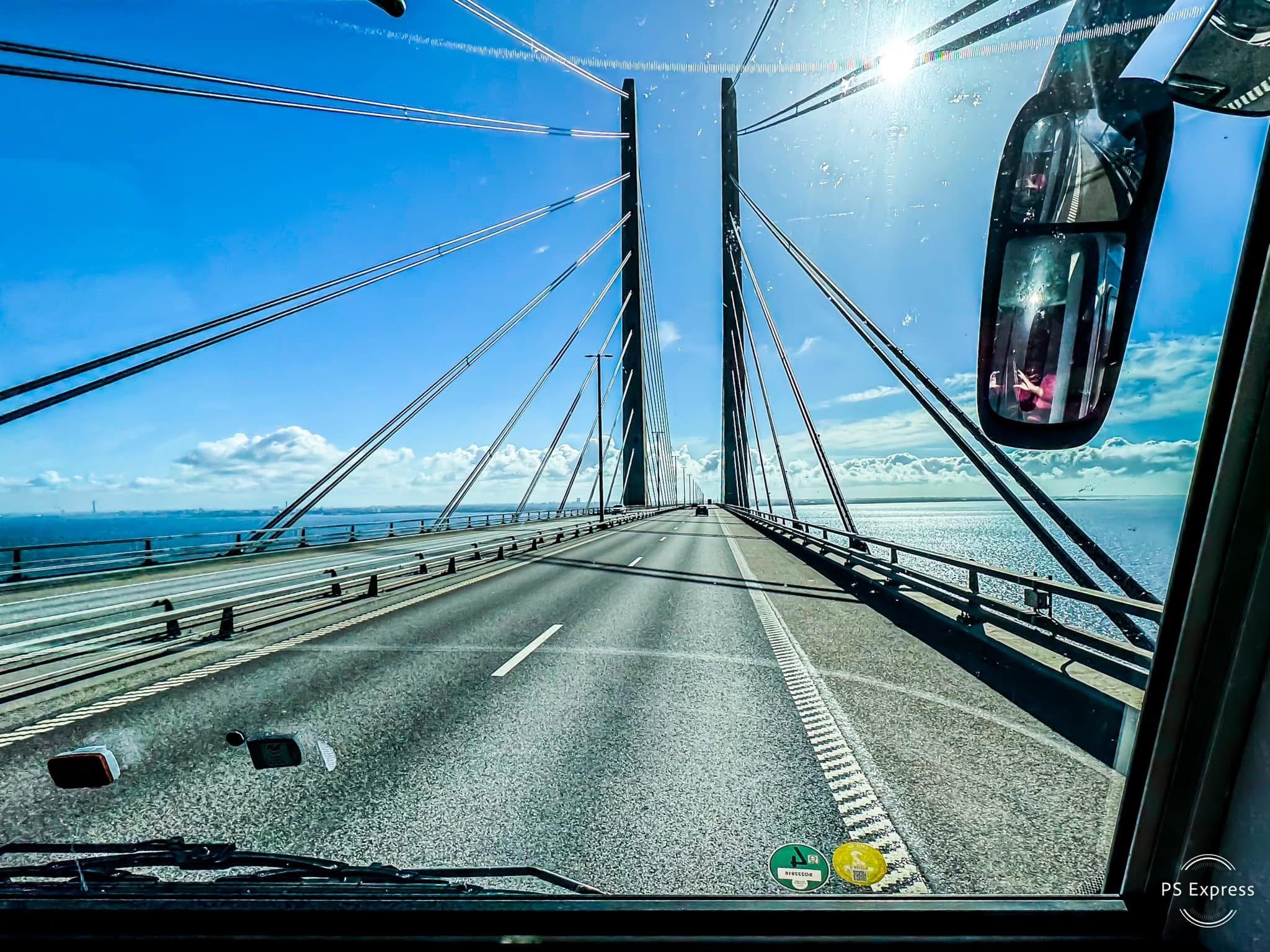 Blick von einem Fahrzeug auf eine Hängebrücke über einem ruhigen Meer bei sonnigem Himmel.