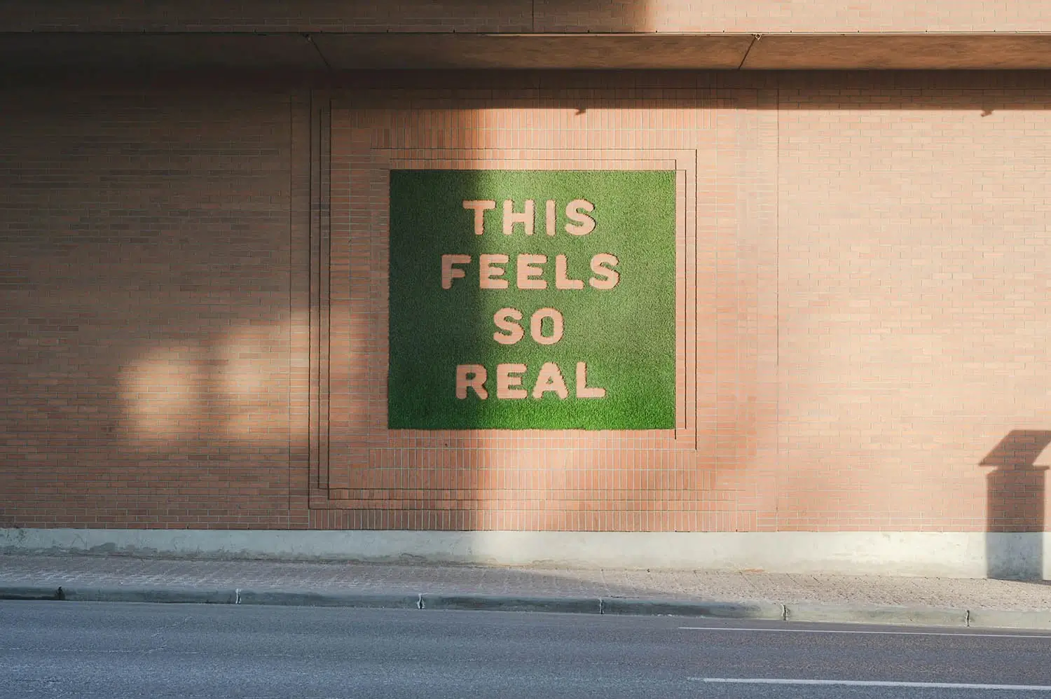 Photograph of a sign painted onto the side of a building in green with the words reading This feels so real