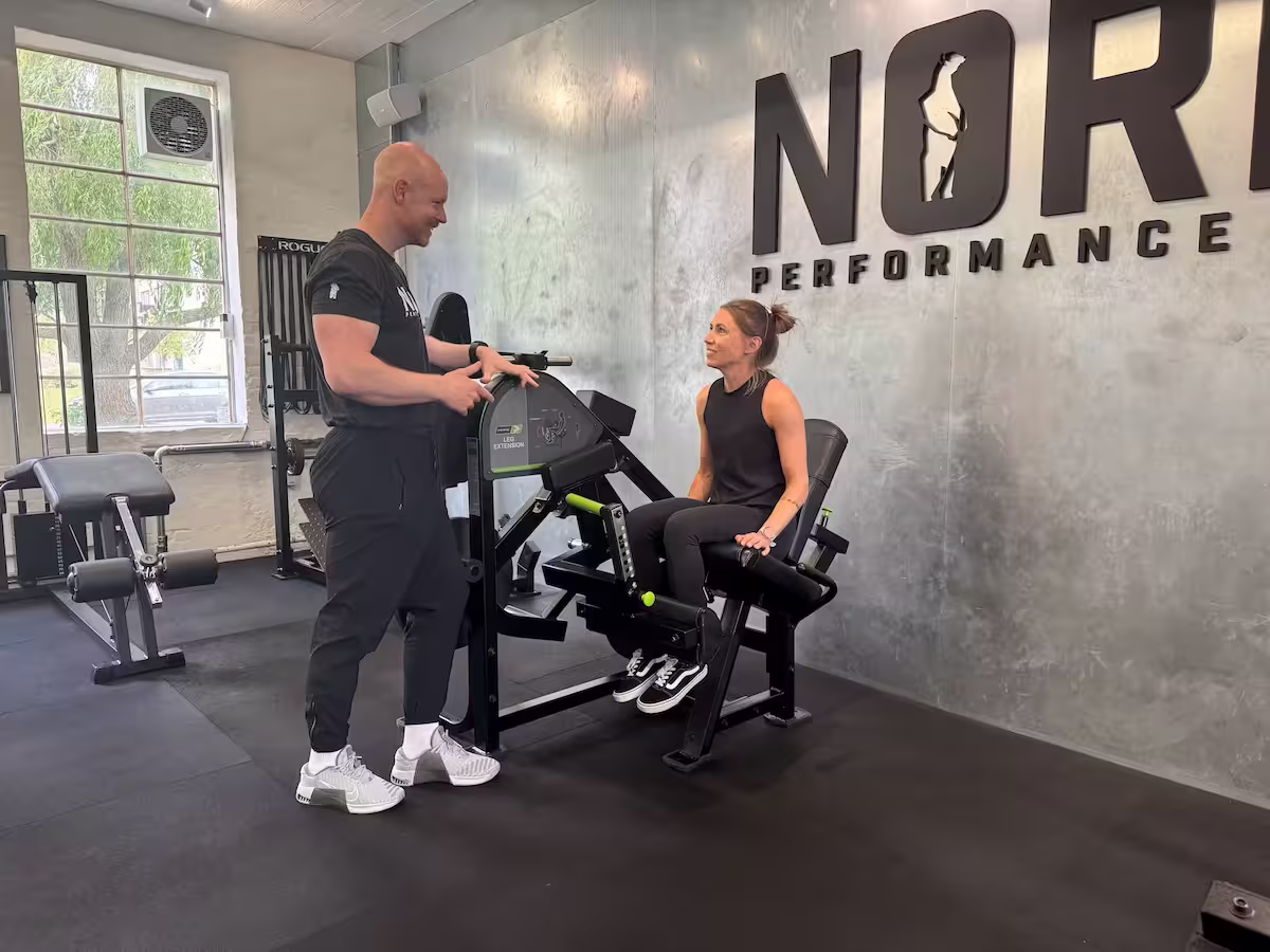 Personal trainer and physiotherapist instructing a client before a set of leg extensions at Nordic Performance Training’s private gym in Copenhagen, emphasizing safety, alignment, and correct form.