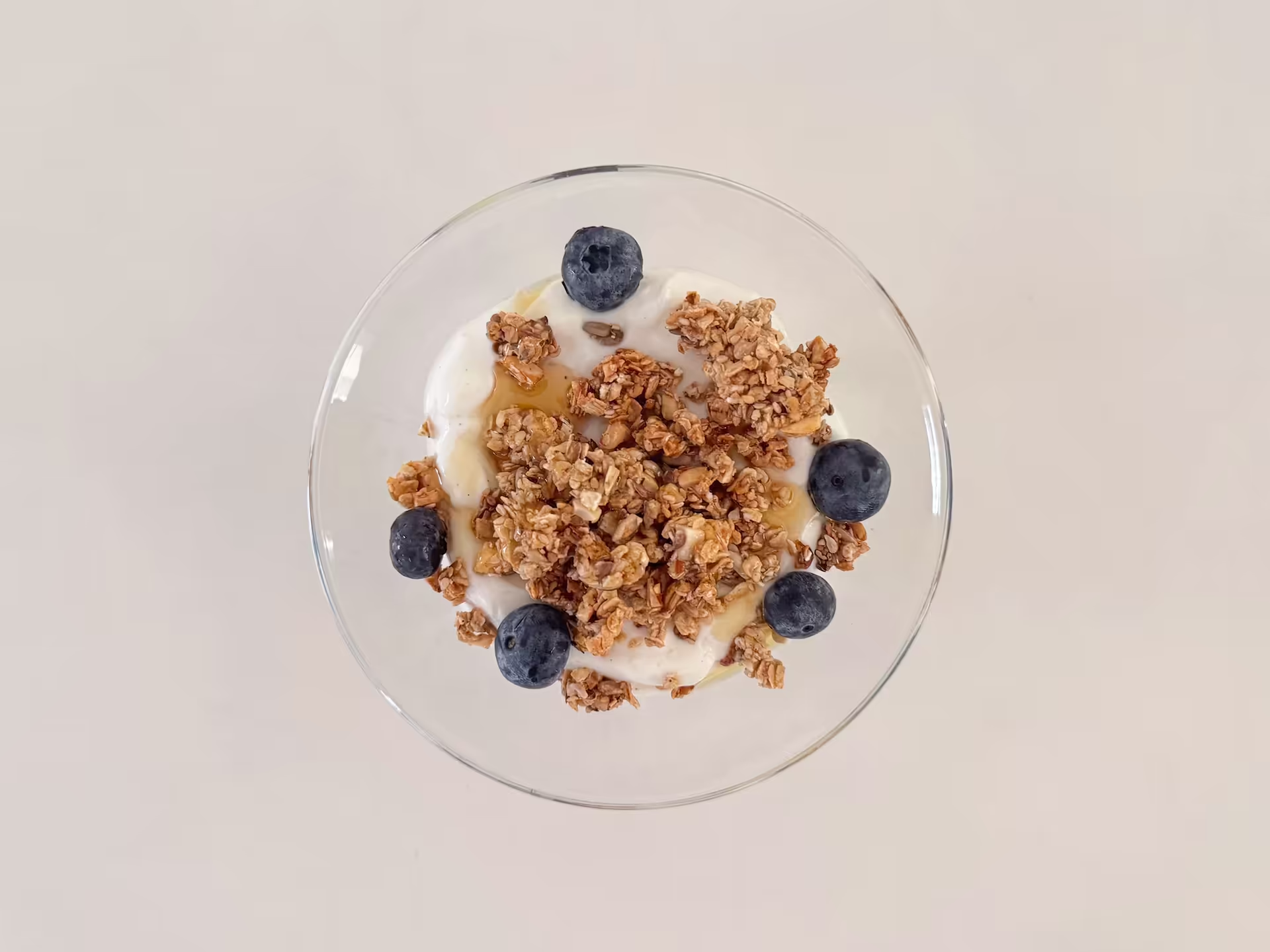 Skål med skyr og proteinrig granola fyldt med nødder, blåbær og honning.