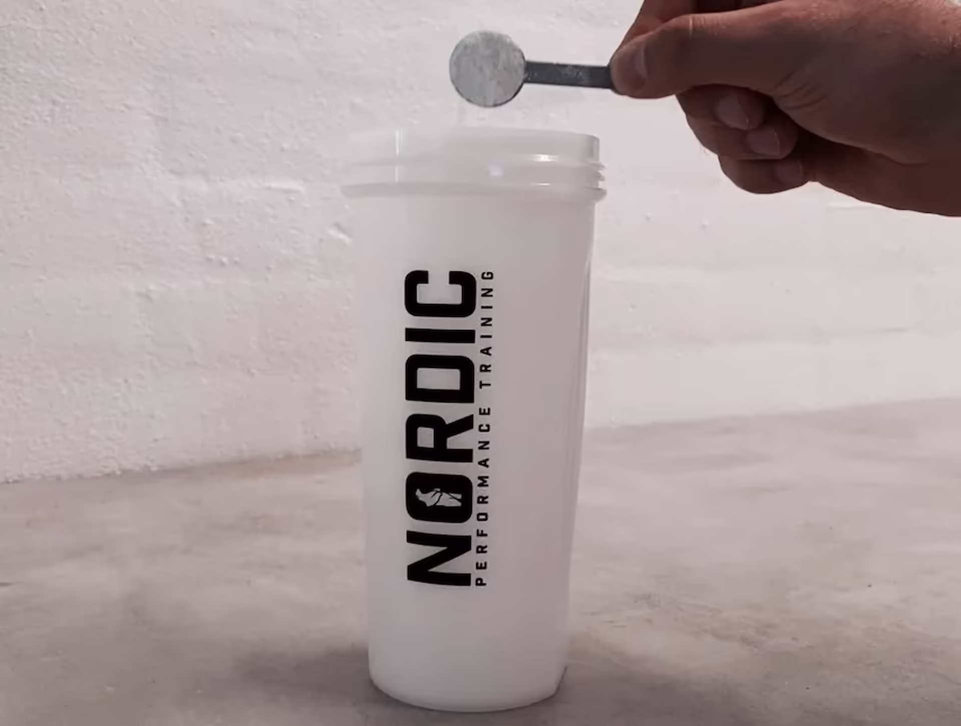 Nordic Performance Training shakerflaske med pre-workout og kosttilskud – indeholder 30–40 g chokoladeproteinpulver, 5 g kreatinmonohydrat (ca. 1 tsk) og 2 tsk kulhydratpulver.